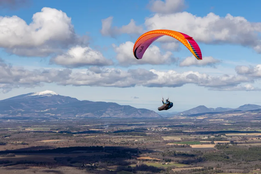 An orange and pink AirDesign Vivo 3 wing and pilot above a mountain landscape